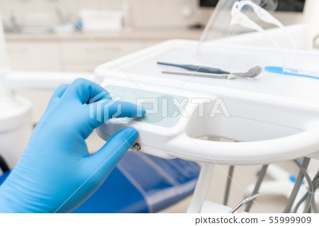 The hand of the dentist in the glove presses the control buttons of the chair.. Dental work in 55999909