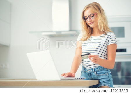 Young blonde woman holding credit card and using 56015295
