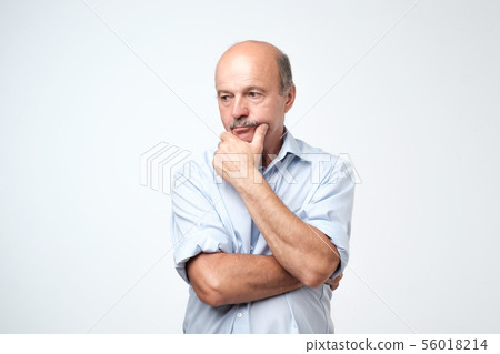 Mature man in blue shirt thinking and looking puzzled. Mature man in blue shirt thinking and looking puzzled. 56018214