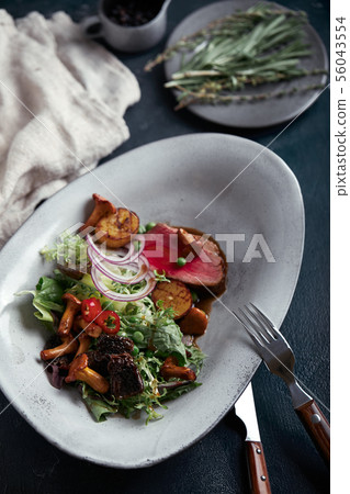 beef tagliata with vegetables. Close-up, low key, gray background. 56043554