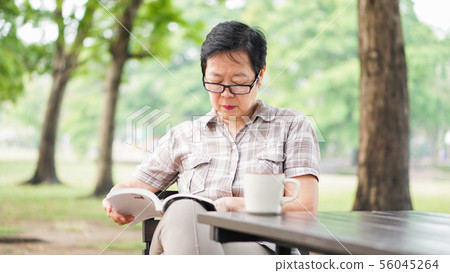 Asian senior woman reading book drinking coffee in Asian senior woman reading book drinking coffee in 56045264