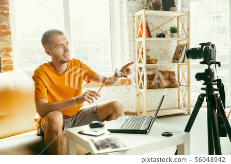 Caucasian male blogger with camera recording video review of gadgets at home Caucasian male blogger with camera recording video review of gadgets at home 56048942