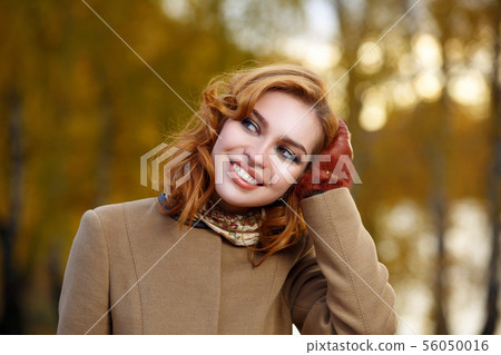 Stylish woman in beige coat and gloves standing in autumn yellow park. Stylish woman in beige coat and gloves standing in autumn yellow park. 56050016