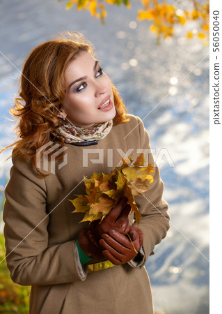 Young woman in the park and holds yellow autumn maple leaves. 56050040