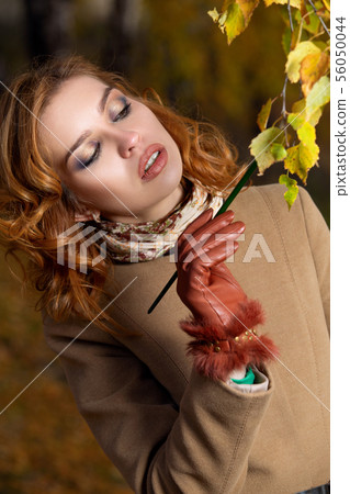 Beautiful woman with palette and brush paints colors leaves on the trees 56050044