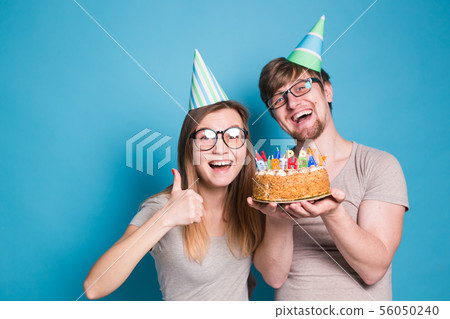 Funny nerd man and woman are wearing holidays caps and glasses holding birthday cake with candles 56050240