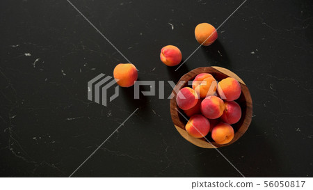 Flat lay photo - apricots in small wooden bowl, on black marble like table, space for text left side 56050817