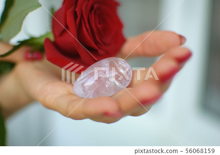 Female hands with manicure holding a yoni egg and red rose. The flower as a symbol of menstruation Female hands with manicure holding a yoni egg and red rose. The flower as a symbol of menstruation 56068159