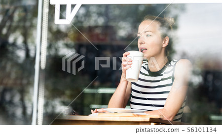 Young caucasian woman sitting alone in coffee shop thoughtfully leaning on her hand, looking trough Young caucasian woman sitting alone in coffee shop thoughtfully leaning on her hand, looking trough 56101134