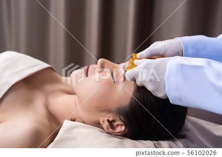 woman receiving traditional guasa face therapy woman receiving traditional guasa face therapy 56102026