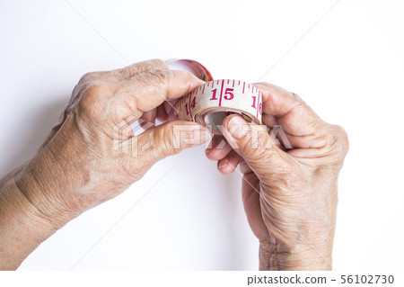 Senior woman's hands coiling tape measure on white 56102730