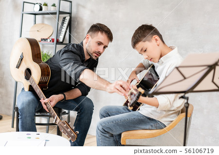 Adult man explains his son, who learn to play guitar, how to play studied chord correctly. Education Adult man explains his son, who learn to play guitar, how to play studied chord correctly. Education 56106719