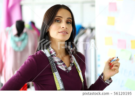 Cheerful female fashion designer holding in arms whiteboard marker Cheerful female fashion designer holding in arms whiteboard marker 56120195