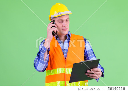 Young man construction worker talking on the phone while holding clipboard 56140236