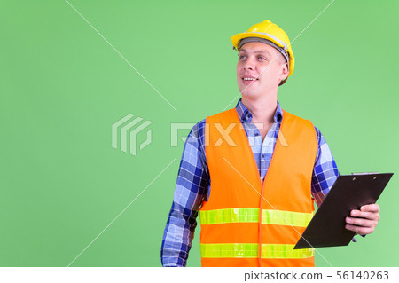 Happy young man construction worker thinking while holding clipboard 56140263