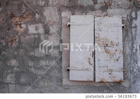 Stone wall and a window with closed shutter 56183673