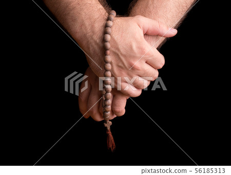 Hands of a male priest with a wooden rosary. 56185313