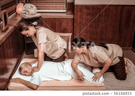 Two masseuses doing their best working with the client. 56188855