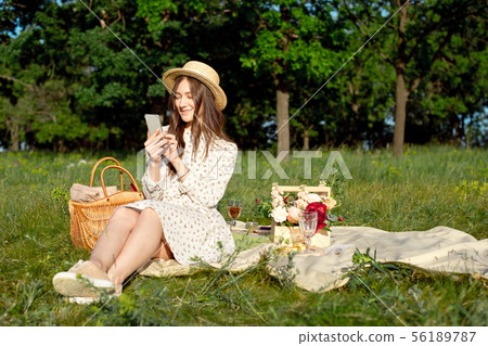 Summer - a picnic in the meadow. girl sitting, reading a book in a smartphone, near a picnic basket 56189787
