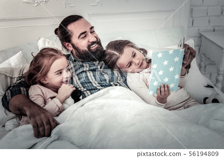 Dad lying in bed with his kids reading story for them Dad lying in bed with his kids reading story for them 56194809