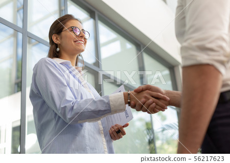 Delighted office worker shaking hands with her partner Delighted office worker shaking hands with her partner 56217623