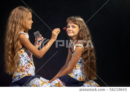 The older sister is applying powder to the younger 56219643