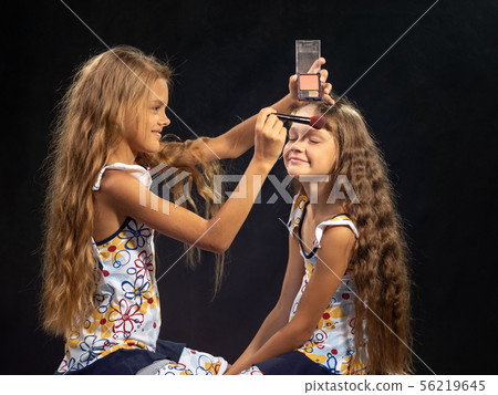 Girl puts powder on the forehead of another girl 56219645