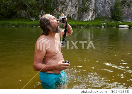 Marure man stands in water with camera. 56241888