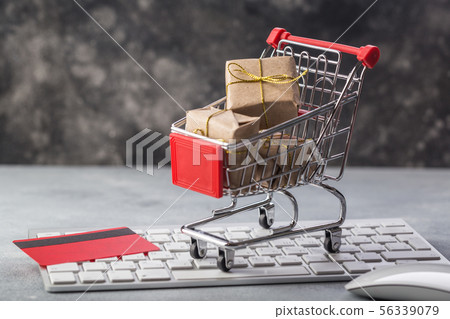 Christmas or New year gift paper box gold ribbon in a small shopping cart on a laptop keyboard Christmas or New year gift paper box gold ribbon in a small shopping cart on a laptop keyboard 56339079
