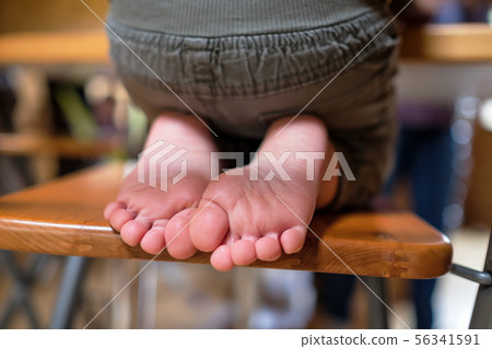 Child is sitting on chair in room. Legs and feet of kids Child is sitting on chair in room. Legs and feet of kids 56341591
