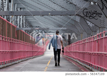 Rear view of unrecognizable stylish young man carrying jeans jacket over his shoulder walking on 56347189