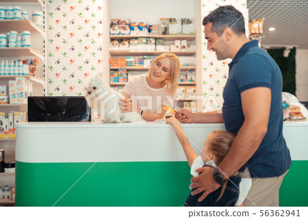 Cashier selling cute white fluffy dog for man with daughter 56362941