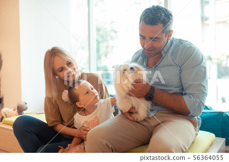 Father holding white fluffy dog sitting near wife and daughter Father holding white fluffy dog sitting near wife and daughter 56364055