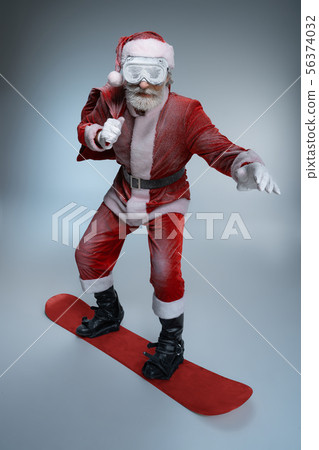 Mature Santa Claus holding sack, standing on snowboard Mature Santa Claus holding sack, standing on snowboard 56374032