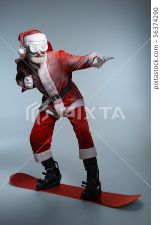 Elderly Santa Claus holding sack, standing on snowboard Elderly Santa Claus holding sack, standing on snowboard 56374290