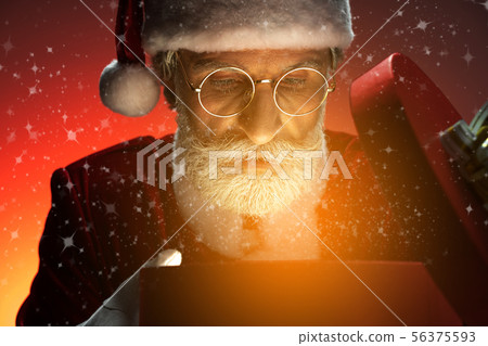 Santa Claus looking at opened gift box with magic light Santa Claus looking at opened gift box with magic light 56375593