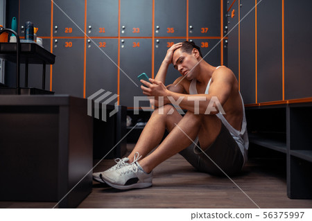 Unhappy cheerless man looking at his smartphone Unhappy cheerless man looking at his smartphone 56375997