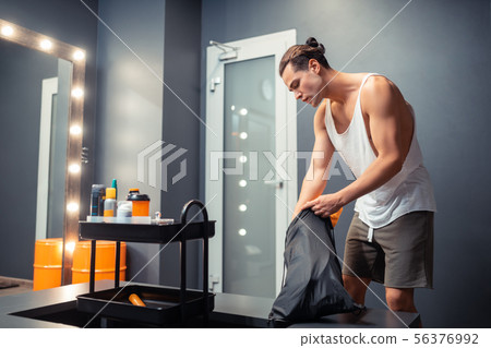 Handsome fit man putting his clothes into the bag Handsome fit man putting his clothes into the bag 56376992