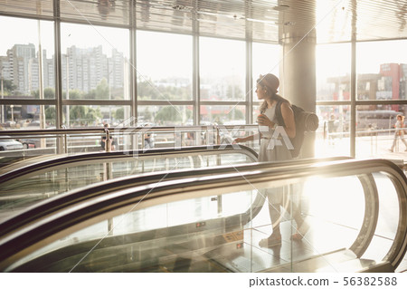 Portrait Smiling Woman Wearing Hat In Airport At Escalator. people traveling with hand luggage 56382588
