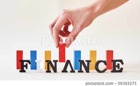 Finance word created with alphabet letters. Hand placing multi-colored wooden blocks in the Finance word created with alphabet letters. Hand placing multi-colored wooden blocks in the 56383271