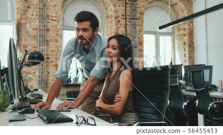 Look here Two young colleagues in casual wear looking at computer monitor and discussing project Look here Two young colleagues in casual wear looking at computer monitor and discussing project 56455453