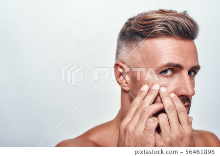 Skin problems. Worried man with a stubble examining his face and looking at camera while standing Skin problems. Worried man with a stubble examining his face and looking at camera while standing 56461898