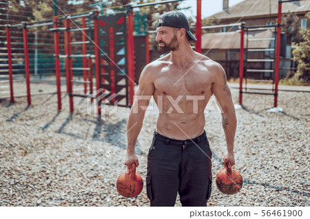 Athletic man working out with a kettlebell at street gym yard. Strength and motivation. 56461900