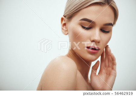 I love my skin. Attractive young blonde woman keeping eyes closed and touching her face while 56462919