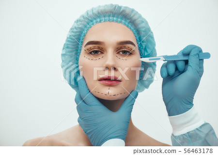 Face lift surgery. Portrait of beautiful young woman in blue medical hat having cosmetic face Face lift surgery. Portrait of beautiful young woman in blue medical hat having cosmetic face 56463178