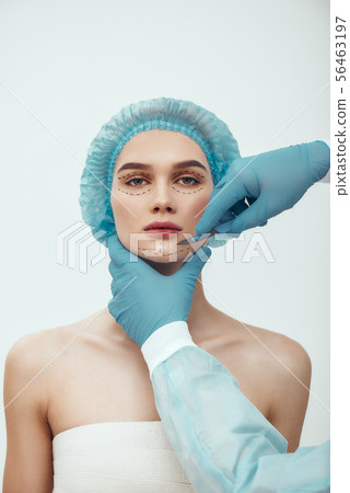 Anti aging treatment. Beautiful young woman in blue medical hat with dashed lines on her face having Anti aging treatment. Beautiful young woman in blue medical hat with dashed lines on her face having 56463197