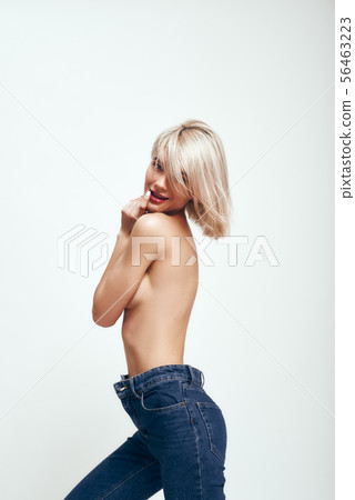 Too sexy. Cute young woman in jeans covering breasts with hands and looking at camera while standing Too sexy. Cute young woman in jeans covering breasts with hands and looking at camera while standing 56463223