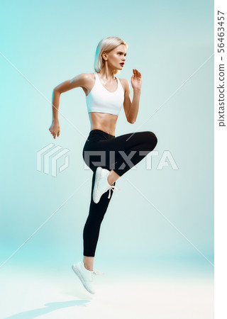 Always in shape. Side view of sporty young woman in white top and black leggings jumping against Always in shape. Side view of sporty young woman in white top and black leggings jumping against 56463457