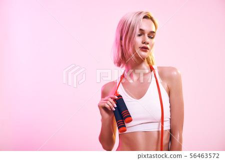 Working out. Sporty healthy woman in white top holding jumping rope and looking aside while standing 56463572
