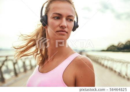 Feeling great. Beautiful young woman in headphones listening music and looking away while standing 56464825